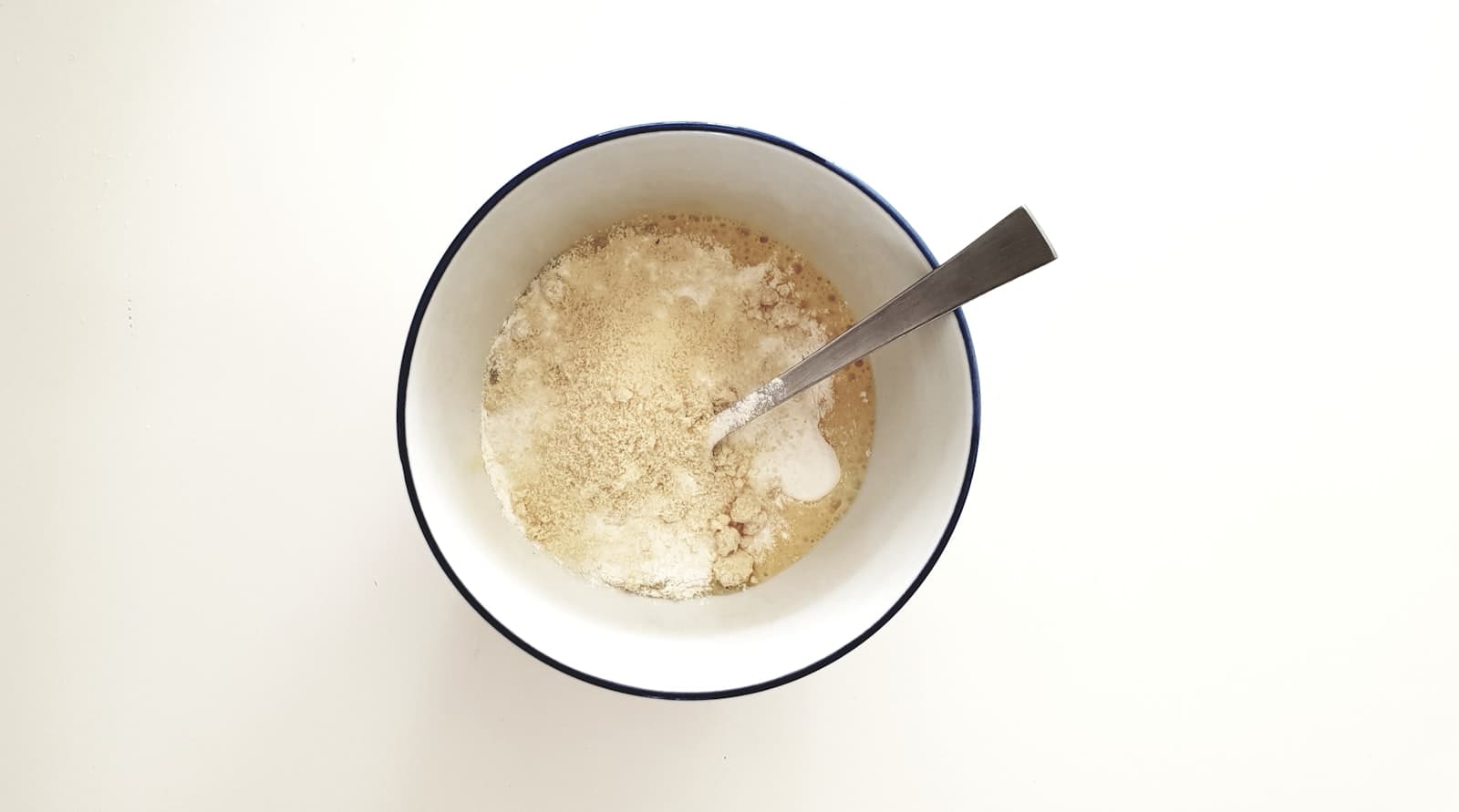 A ceramic bowl of flour with a metal spoon