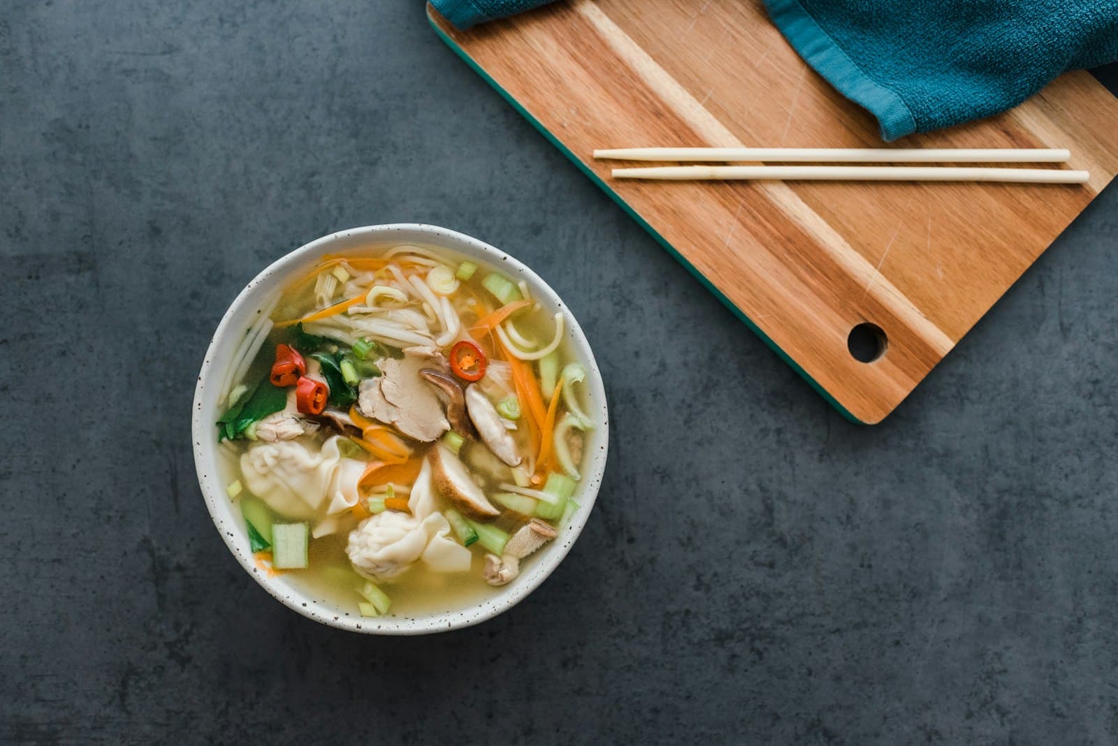 A white ceramic bowl of chicken soup with wooden chopsticks