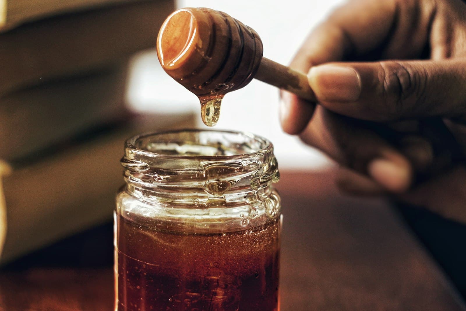 Honey dripping from a dipper into a jar beside honeycomb